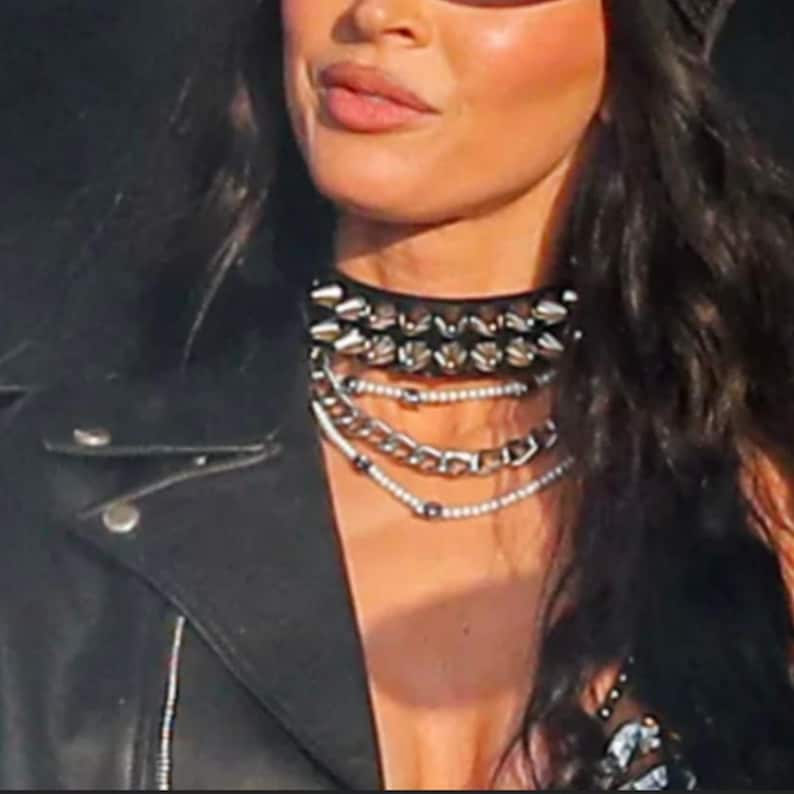 May include: A woman wearing a black leather jacket with a silver and black studded choker necklace.