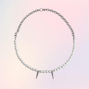 May include: A silver chain necklace with a row of white pearls and two silver spikes at the bottom.