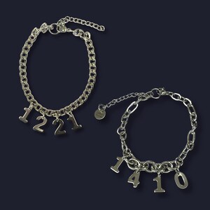 May include: Two silver-toned chain bracelets. One bracelet has the numbers "1221" as charms. The other bracelet has the numbers "1410" as charms. Both bracelets have an adjustable chain closure.