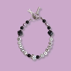 May include: A black and silver beaded bracelet with the words "Hotel Diablo" spelled out in silver beads. The bracelet also features black and white dice charms and a silver key charm.