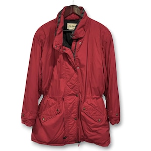 Puede incluir: Chaqueta roja L.L.Bean con interior negro y cintura con cordón. La chaqueta tiene cremallera, bolsillos abotonados y cuello alto. La chaqueta está colgada de una percha de madera.