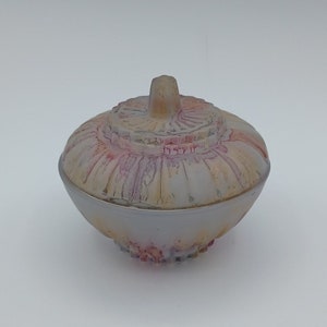 Puede incluir: Una pequeña caja de cerámica blanca con tapa. La tapa tiene un diseño floral en relieve en tonos rosa y amarillo. La caja mide aproximadamente 7,5 cm de alto.