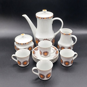 May include: A white porcelain tea set with a brown and orange floral pattern. The set includes a teapot, creamer, sugar bowl, and four cups and saucers.