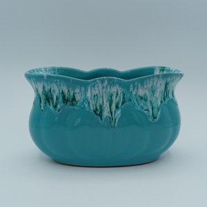 May include: A turquoise ceramic planter with a scalloped rim. The rim has a white and green glaze that drips down the sides. The planter has a rounded shape and a glossy finish, suitable for indoor or outdoor use.