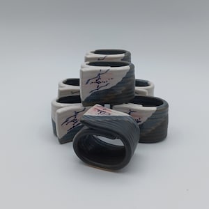 Puede incluir: Un conjunto de anillos de servilleta de cerámica con un diseño azul y blanco. Los anillos están apilados en forma de pirámide, con el anillo superior de color gris oscuro.