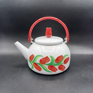 May include: White enamel teapot with a red handle and tulip design. The teapot has a red tulip-shaped knob on the lid and a curved spout. Red tulips and green leaves are painted around the body of the teapot.