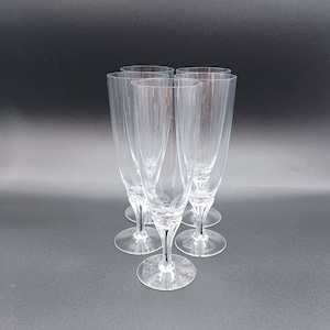 May include: Set of five clear glass champagne flutes with a tall, slender design. The flutes have a delicate, elegant appearance.