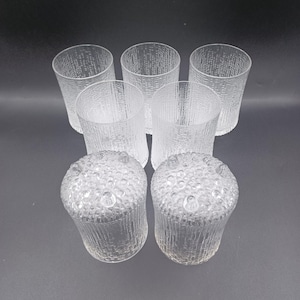 May include: A set of six clear glass tumblers and two matching candle holders. The glasses have a textured, vertical lined design. The candle holders have a textured, bubble-like design on the top and sides.