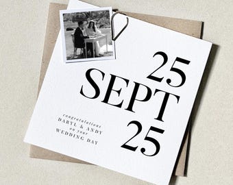 May include: A wedding card with the date "25 SEPT 25" in large black font. A small black and white photo of a couple is attached with a paper clip. The card also includes the text "congratulations DARYL & ANDY on your WEDDING DAY."