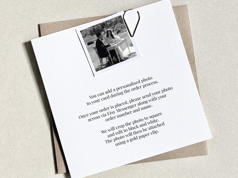 K&ouml;nnte beinhalten: Eine wei&szlig;e Karte mit einem Schwarz-Wei&szlig;-Foto eines Paares, befestigt mit einer goldenen B&uuml;roklammer. Text auf der Karte erkl&auml;rt, wie man ein personalisiertes Foto zu einer Bestellung hinzuf&uuml;gt. Die Karte liegt auf einem braunen Umschlag.