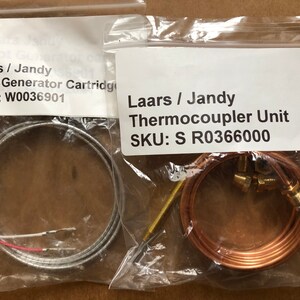 May include: Two packages containing replacement parts for a gas fireplace. The package on the left contains a silver pilot generator cartridge with the SKU W0036901. The package on the right contains a copper thermocouple unit with the SKU S R0366000.