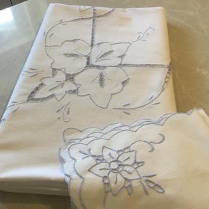 Pode incluir: Toalha de mesa branca bordada com um desenho floral. A toalha de mesa é feita de linho e tem um padrão delicado e intrincado. A toalha de mesa é perfeita para um jantar formal ou uma ocasião especial.