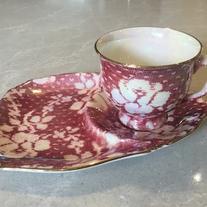 May include: A red and white teacup and saucer set with a floral pattern. The set has a gold trim around the edges.