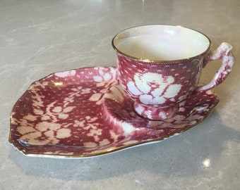 May include: A red and white teacup and saucer set with a floral pattern. The set has a gold trim around the edges.
