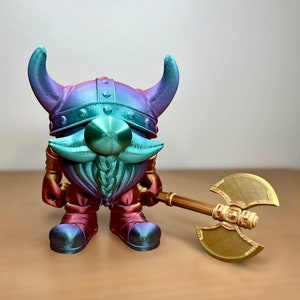 May include: A colorful, 3D-printed gnome figurine with a Viking helmet and a large double-bladed axe. The gnome's helmet and beard are teal, purple, and blue. The axe is gold and brown. The figurine is approximately 6 inches tall.