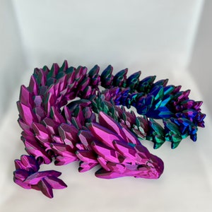 May include: A 3D printed dragon sculpture with a iridescent purple and green finish. The dragon is curled up in a sleeping position with its head resting on its tail.
