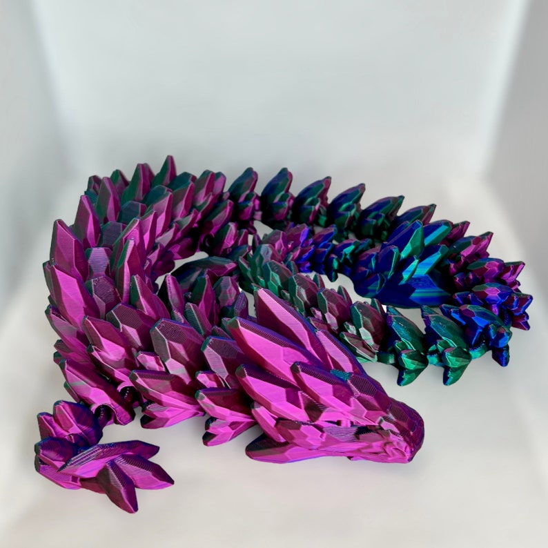 May include: A 3D printed dragon sculpture with a iridescent purple and green finish. The dragon is curled up in a sleeping position with its head resting on its tail.