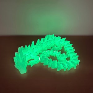 May include: A glowing green dragon figurine made of plastic. The dragon is curled up in a sleeping position with its head resting on its tail.