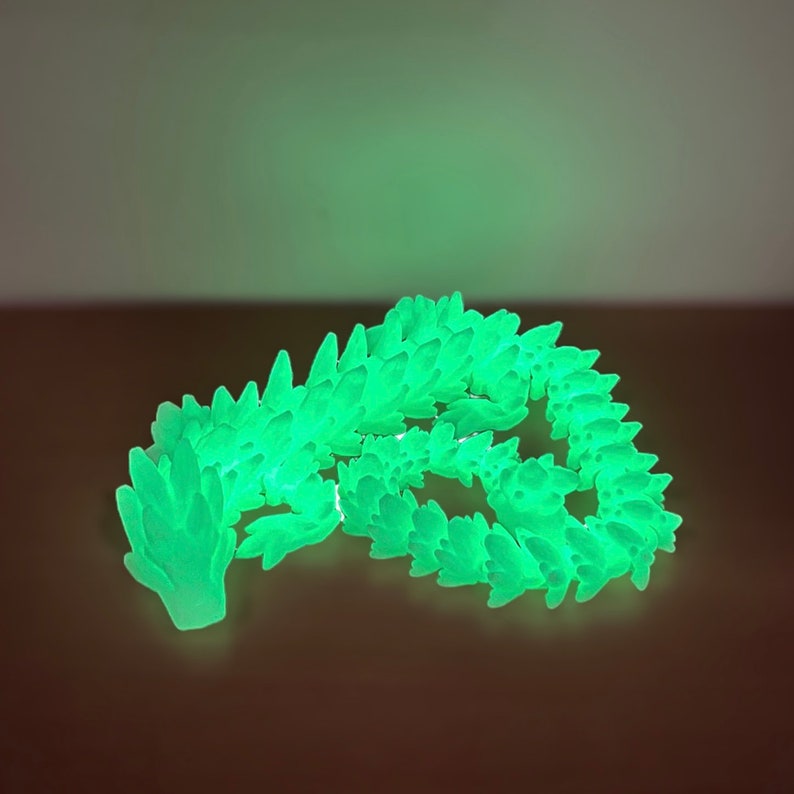 May include: A glowing green dragon figurine made of plastic. The dragon is curled up in a sleeping position with its head resting on its tail.