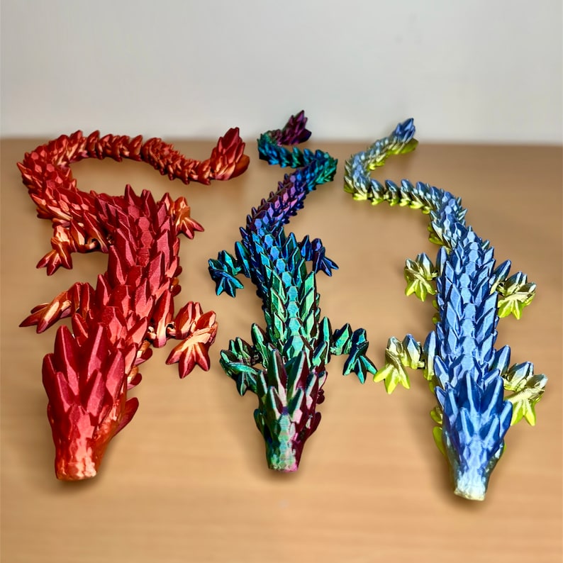 May include: Three iridescent dragon figurines, one red, one green, and one blue. Each dragon is made of a shiny, scaly material and has a long tail and a pointed snout.