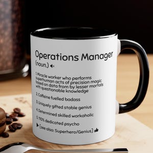 May include: A white ceramic mug with a black interior and handle. The mug features the text "Operations Manager (noun.)" along with a humorous definition. The mug is a standard 11 oz size.
