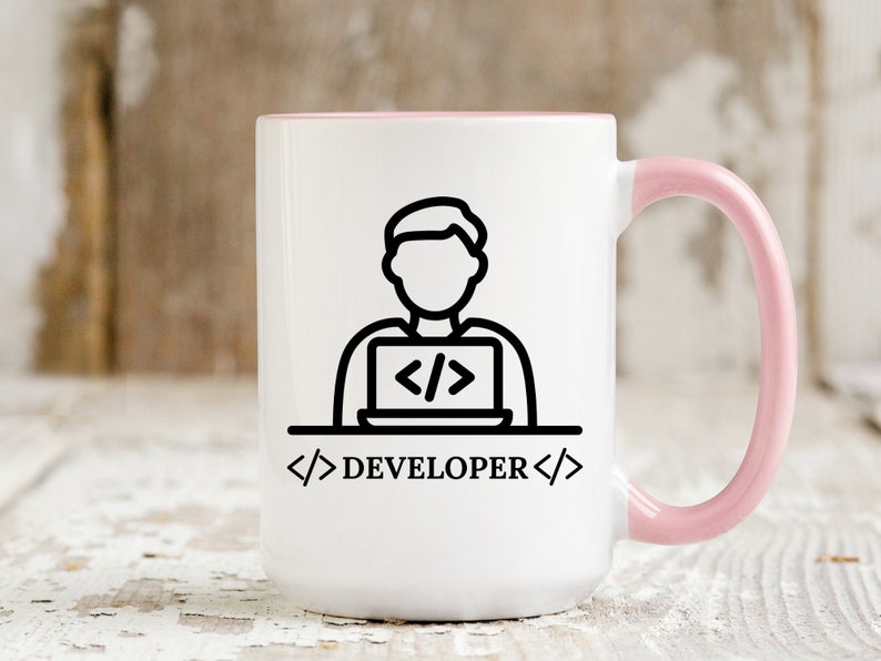 May include: White coffee mug with a pink interior and handle. The mug features a black line drawing of a person working on a laptop, with the word "DEVELOPER" below. The design is simple and modern.