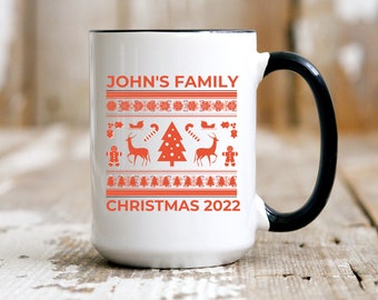 May include: White ceramic mug with a black handle and rim, featuring a festive orange Christmas design. The design includes reindeer, a Christmas tree, and the text "JOHN'S FAMILY CHRISTMAS 2022".