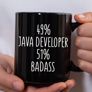 May include: Black coffee mug with the text "49% JAVA DEVELOPER 51% BADASS" in white. The mug is held by a person.
