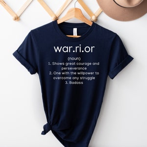 Peut inclure: Un t-shirt bleu marine avec du texte blanc qui dit "war.ri.or (nom) 1. Montre un grand courage et de la persévérance 2. Quelqu'un qui a la volonté de surmonter n'importe quelle difficulté 3. Badass"