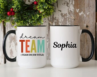 May include: Two white ceramic mugs with black handles. One mug has the text "dream TEAM (TEAM OR JOB TITLE)" in colorful letters. The other mug has the name "Sophia" in black cursive.