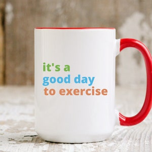 May include: White ceramic mug with a red handle and interior. The mug features the text "it's a good day to exercise" in green, blue, and orange. A motivational item for fitness enthusiasts.