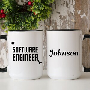 Puede incluir: Dos tazas de cer&aacute;mica blancas con asas y bordes negros. Una taza dice "SOFTWARE ENGINEER" en letras negras en negrita con acentos de flecha. La otra taza tiene el nombre "Johnson" en una fuente de escritura.