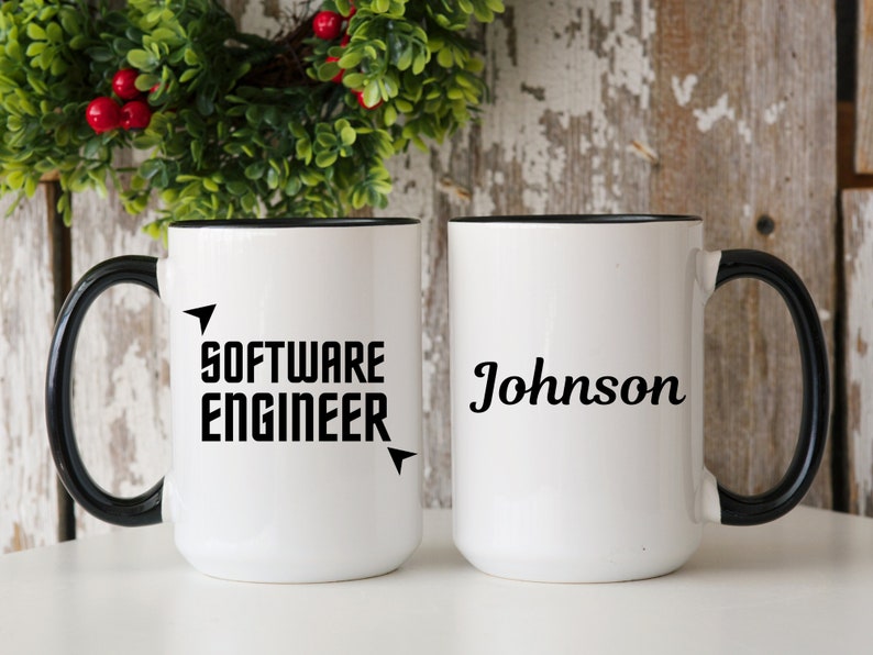 Puede incluir: Dos tazas de cer&aacute;mica blancas con asas y bordes negros. Una taza dice "SOFTWARE ENGINEER" en letras negras en negrita con acentos de flecha. La otra taza tiene el nombre "Johnson" en una fuente de escritura.