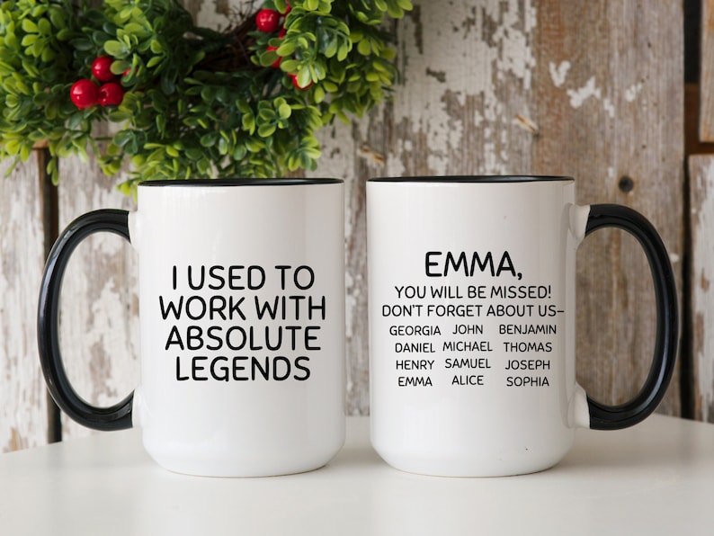 May include: Two white coffee mugs with black handles and black rims. The mug on the left says "I used to work with absolute legends". The mug on the right says "Emma, you will be missed! Don't forget about us - Georgia John Benjamin Daniel Michael Thomas Henry Samuel Joseph Emma Alice Sophia".
