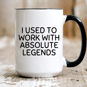 May include: White ceramic coffee mug with a black rim and handle. The mug has black text that reads "I used to work with absolute legends".