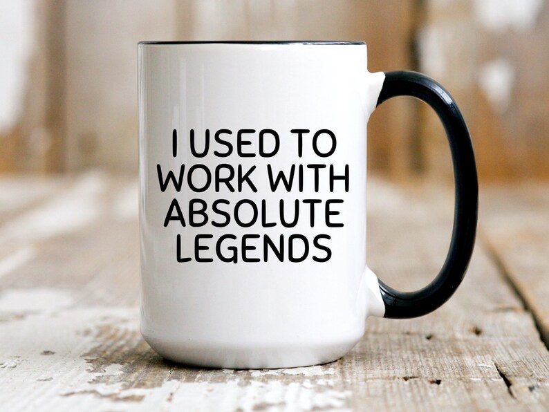 May include: White ceramic coffee mug with a black rim and handle. The mug has black text that reads "I used to work with absolute legends".