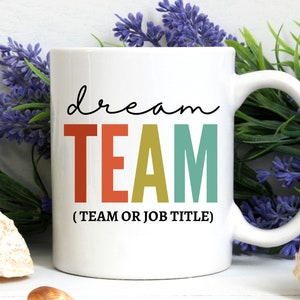 May include: White ceramic coffee mug with the text "dream TEAM (TEAM OR JOB TITLE)" in colorful letters. The letters are in shades of red, orange, yellow, and green.