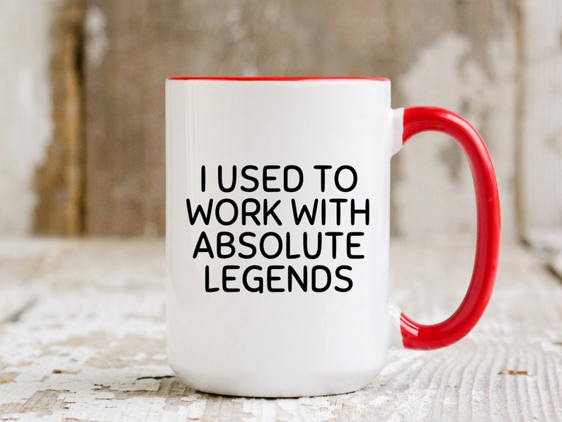 May include: White ceramic mug with a red rim and handle. The mug has black text that reads "I used to work with absolute legends."