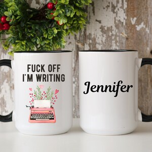 May include: White ceramic mug with a black handle and rim. One side features the text "FUCK OFF I'M WRITING" above a pink typewriter illustration. The other side displays the name "Jennifer" in black script. A perfect gift for writers.