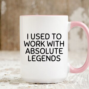 May include: White ceramic coffee mug with a pink rim and handle. The mug has black text that reads "I used to work with absolute legends."