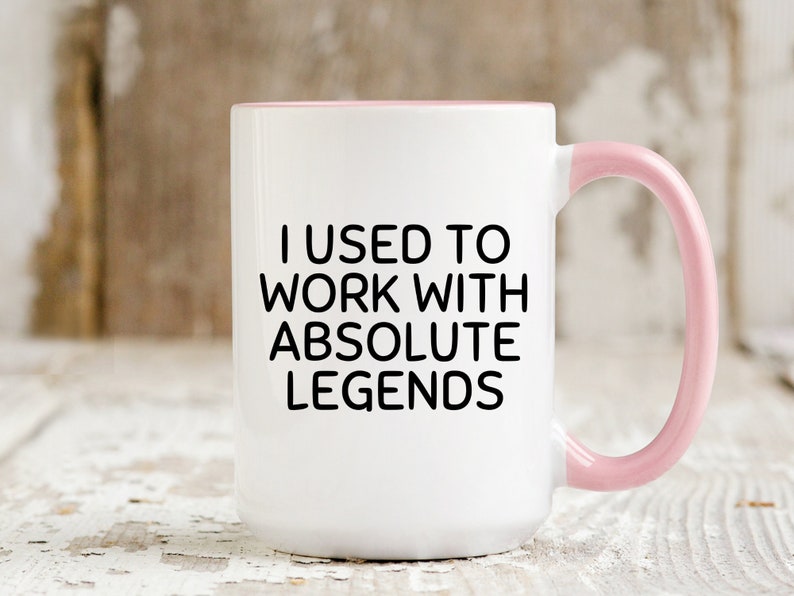 May include: White ceramic coffee mug with a pink rim and handle. The mug has black text that reads "I used to work with absolute legends."