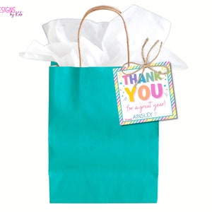 Puede incluir: Una bolsa de regalo turquesa con papel de seda blanco y una etiqueta de agradecimiento colorida que dice "Gracias por un gran a&ntilde;o! De Ainsley".
