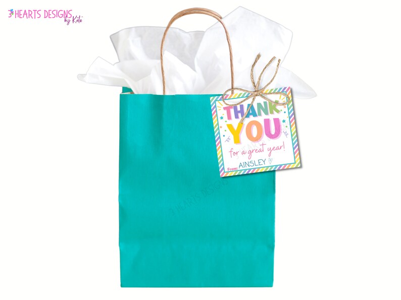 Puede incluir: Una bolsa de regalo turquesa con papel de seda blanco y una etiqueta de agradecimiento colorida que dice "Gracias por un gran a&ntilde;o! De Ainsley".