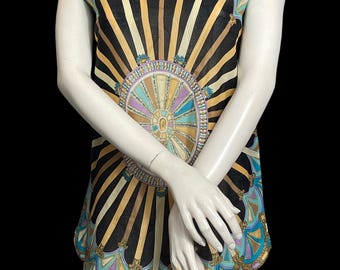 May include: A sleeveless tunic top featuring a black background with a central circular medallion and radiating gold, teal, and lavender architectural columns. The garment has a boat neckline and a scalloped hemline with decorative gold trim.
