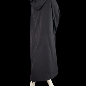 May include: A long, black hooded coat. The coat has a drawstring waist and a long, flowing skirt. The hood is large and covers the head. The coat is made of a lightweight material and appears to be suitable for layering.