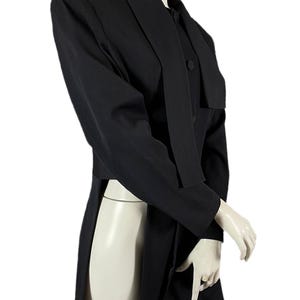 May include: A black blazer with a unique design, featuring a long, flowing panel on the front and a notched lapel. The blazer has long sleeves and a button closure. The garment is displayed on a mannequin.