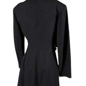 May include: A black blazer with long sleeves, a notched collar, and a flared hem. The back view of the blazer shows a tailored fit, emphasizing the waist. The garment is displayed on a mannequin against a white background.