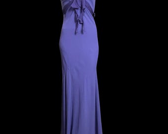 May include: A floor-length purple sleeveless dress featuring a deep V-neckline with a gathered fabric tie detail at the centre chest. The dress has a fitted bodice that transitions into a slightly flared skirt, creating a long, flowing silhouette.