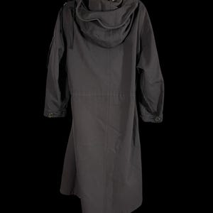 May include: A long, dark gray coat with a large hood, hanging on a black hanger. The coat has a button closure and pockets. The coat is made of a durable material.
