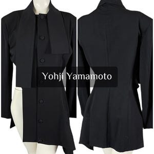 May include: Black Yohji Yamamoto jacket with a unique asymmetrical design. The jacket features a high collar, long sleeves, and a button-up front. The text "Yohji Yamamoto" is displayed on the image.